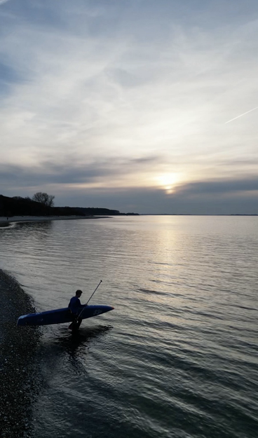 Paddler trägt sein Board an der Ostsee ins Wasser
