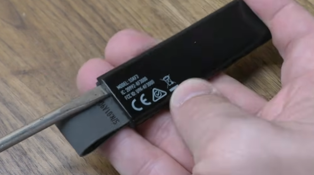 Still frame from a video depicting a screwdriver prying open a SimpliSafe key fob.