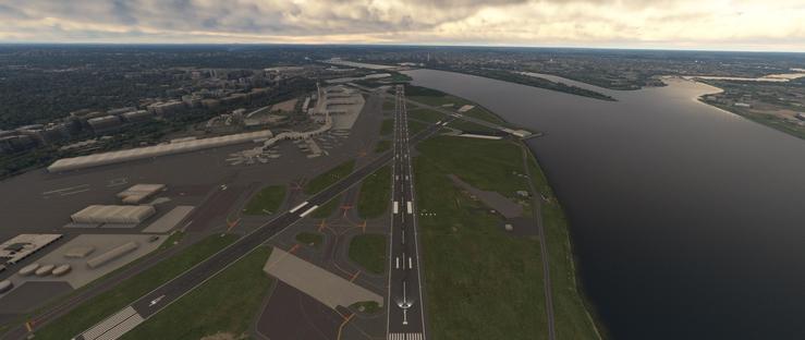 Aerial view of a large airport featuring a prominent central runway running toward a significant water body. The airport includes multiple taxiways, terminal structures including a distinctive star-shaped building, and ground support facilities. Surrounding the airfield are green areas, smaller buildings, and a coastal cityscape with dense urban development stretching into the distance. The waterway, with visible islands, borders the airport on one side, while the horizon shows a sprawling metropolitan area under an overcast sky with layered clouds. The scene captures the layout of a major aviation hub situated between land and water, with infrastructure facilitating aircraft operations and urban integration.