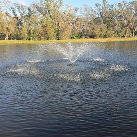 Powerful pond fountains spraying water in a wide circular pattern across a large outdoor pond.