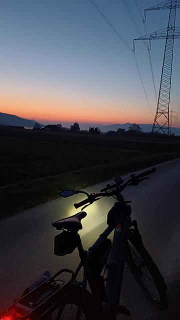 Fahhrad steht beleuchtet auf einem Weg. Im Hintergrund zeigt sich das Morgenrot im Tal.