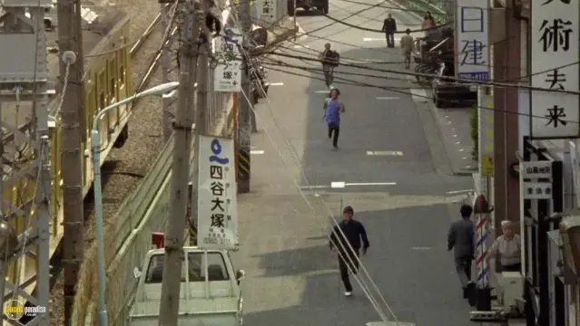 Frame from a movie “Dangan Runner”. Three man running down the street in Tokyo one after another.