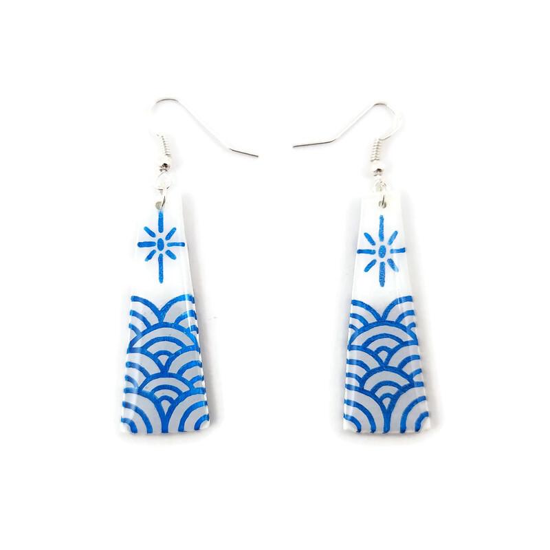 Boucles d'oreilles fantaisie pendantes en forme de longs trapèzes blancs ornés de vagues et d'un soleil stylisés bleus métallisés.
Les perles sont réalisées en CD recyclé, découpées et peintes à la main, puis recouvertes de résine époxy.
Les crochets sont en métal argenté, mais sont disponibles dans d'autres coloris et métaux.