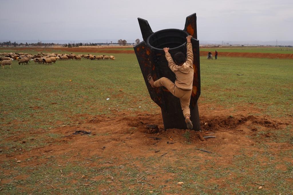A boy tries to climb on an unexploded Iranian missile that landed in an open field.