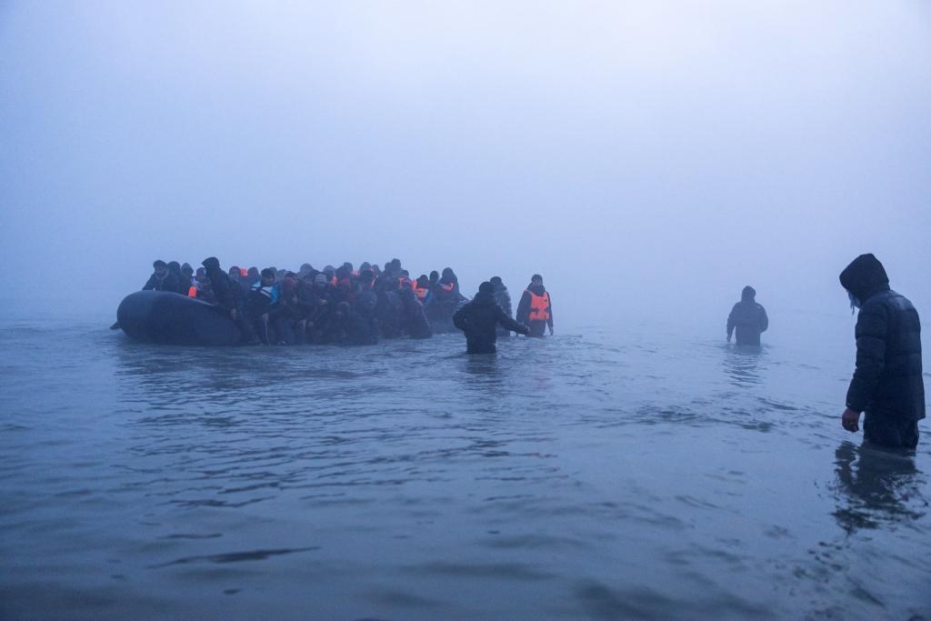 Smugglers assist migrants in boarding a boat as they attempt to cross the English Channel off the beach of Gravelines.