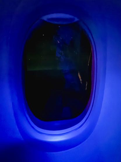 An airplane window with blue interior lighting and faint aurora outside