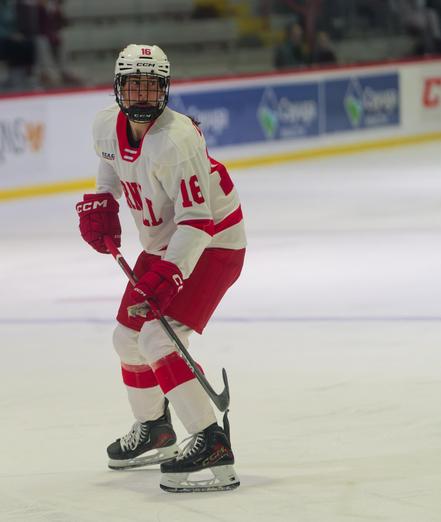 Partially crouching hockey player #16 wearing white clothes with red shorts seemingly by herself on the ice.