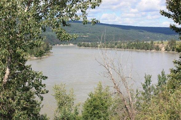 A broad smooth section of river surrounded by trees and hills, with rocky shorelines along the river itself.