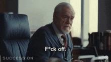 Logan Roy sitting at his desk with a sweater shirt and tie saying "fuck off"