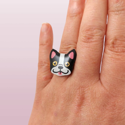 Bague fantaisie éco-responsable en forme de tête de bouledogue français noir et blanc.
La perle est réalisée en CD recyclé, découpée et peinte à la main, puis recouverte de résine.
L'anneau en acier inoxydable est réglable, et est disponible en doré ou argenté.
La bague est portée à l'annulaire d'une main gauche, devant un fond rose clair.