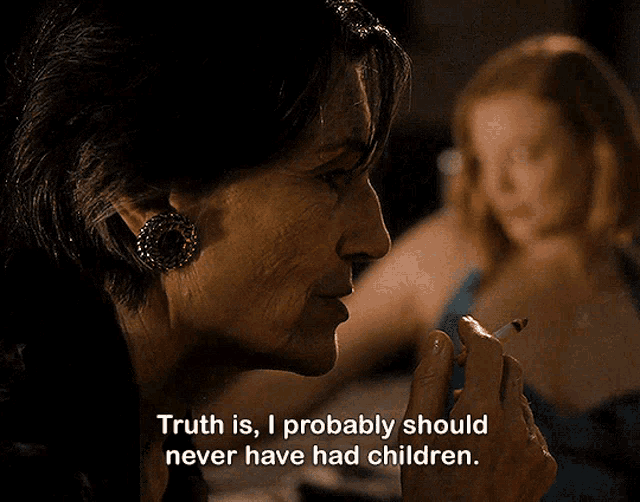 Caroline smoking a cigarette. Shiv is in the background unfocused. "Truth is, I probably should never have had children"