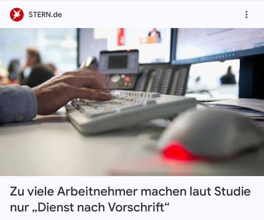 Das Bild zeigt eine Nahaufnahme eines Büroarbeitsplatzes. Im Vordergrund befindet sich eine Hand, die auf einer weißen Tastatur tippt, eine Computermaus mit einem roten Licht, und ein mehrzeiliges Bürotelefon. Hinter der Tastatur befinden sich Computerbildschirme. Im Hintergrund sind verschwommene Personen und weitere Bürobildschirme zu sehen. In der oberen linken Ecke befindet sich das Logo "STERN.de" mit einem roten Stern-Symbol. Der Text am unteren Rand lautet: "Laut einer Studie erledigen zu viele Arbeitnehmer nur 'Dienst nach Vorschrift'."
