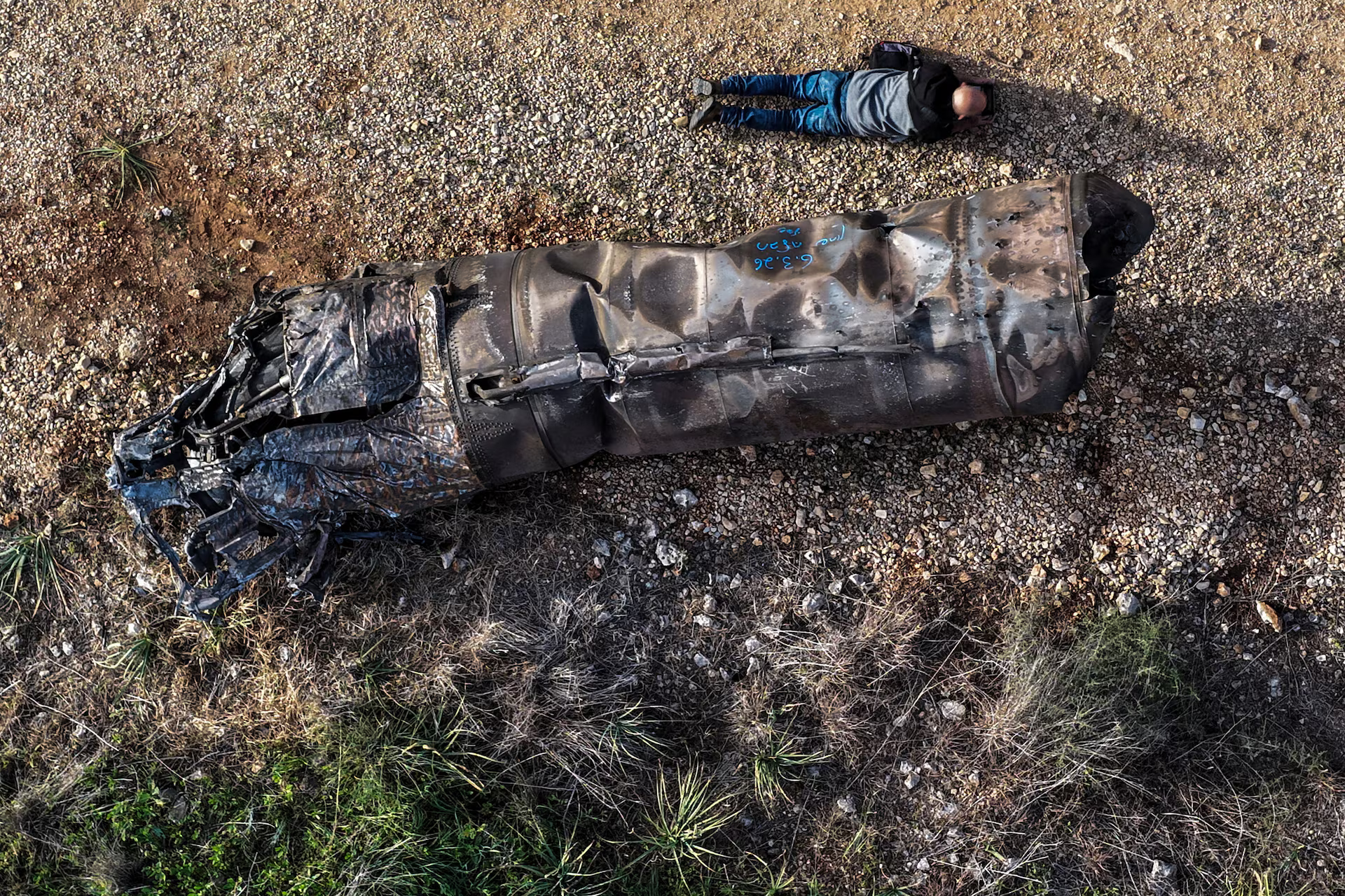 A drone view shows a drone operator taking a picture of the remains of a missile.