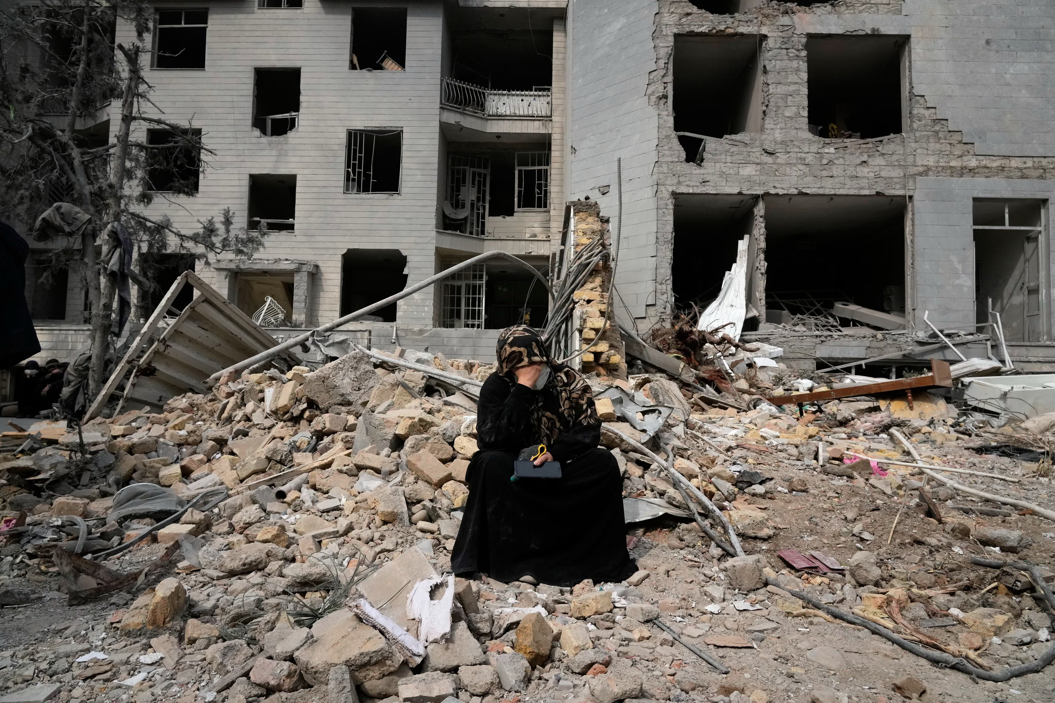 A woman sits on rubble by a residential building damaged by the US-Israeli bombing campaign.