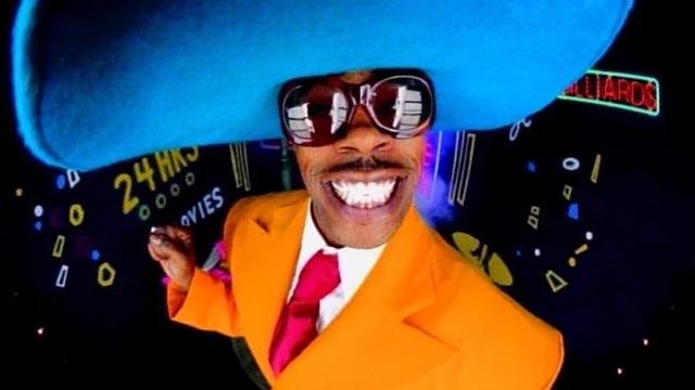 Busta Rhymes wearing a large blue hat and neon orange suit