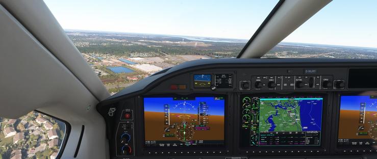 Inside an aircraft cockpit, the main display panels show active flight instruments and navigation data. Three primary screens dominate the panel: the left screen features an attitude indicator with a heading of 319 degrees, a glide slope indicator, and altitude information; the central screen displays a map with green terrain, blue water bodies, and navigation details including Approach - KCRG-ILS-32 and Active Nav; the right screen mirrors the left with similar metrics. Knobs and switches on the panel are labeled with functions like HDG, ALT SEL, CRS, and D-MJXY is visible near the top. Outside the cockpit, the windshield reveals a clear view of a landscape with suburban residential areas, industrial buildings, a large runway, and multiple bodies of water under a bright sky. The aircraft is approaching a landing, as indicated by the navigation data and runway alignment.