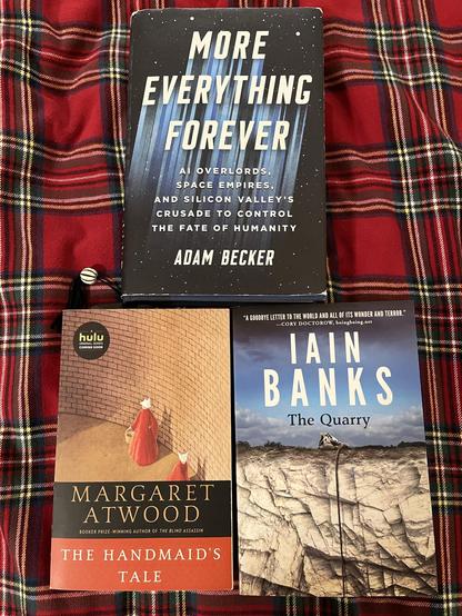 There are three books lying flat on my red and green, tartan duvet—the topmost book being Adam Becker’s More Everything Forever while the bottom two, from left to right are Margaret Atwood’s The Handmaid’s Tale and Iain Banks’s The Quarry.