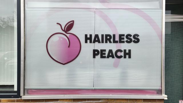 A shop window with the business name "Hairless Peach", and the heart-shaped logo, inspired by a peach, with a small stem and a single, small leaf.
