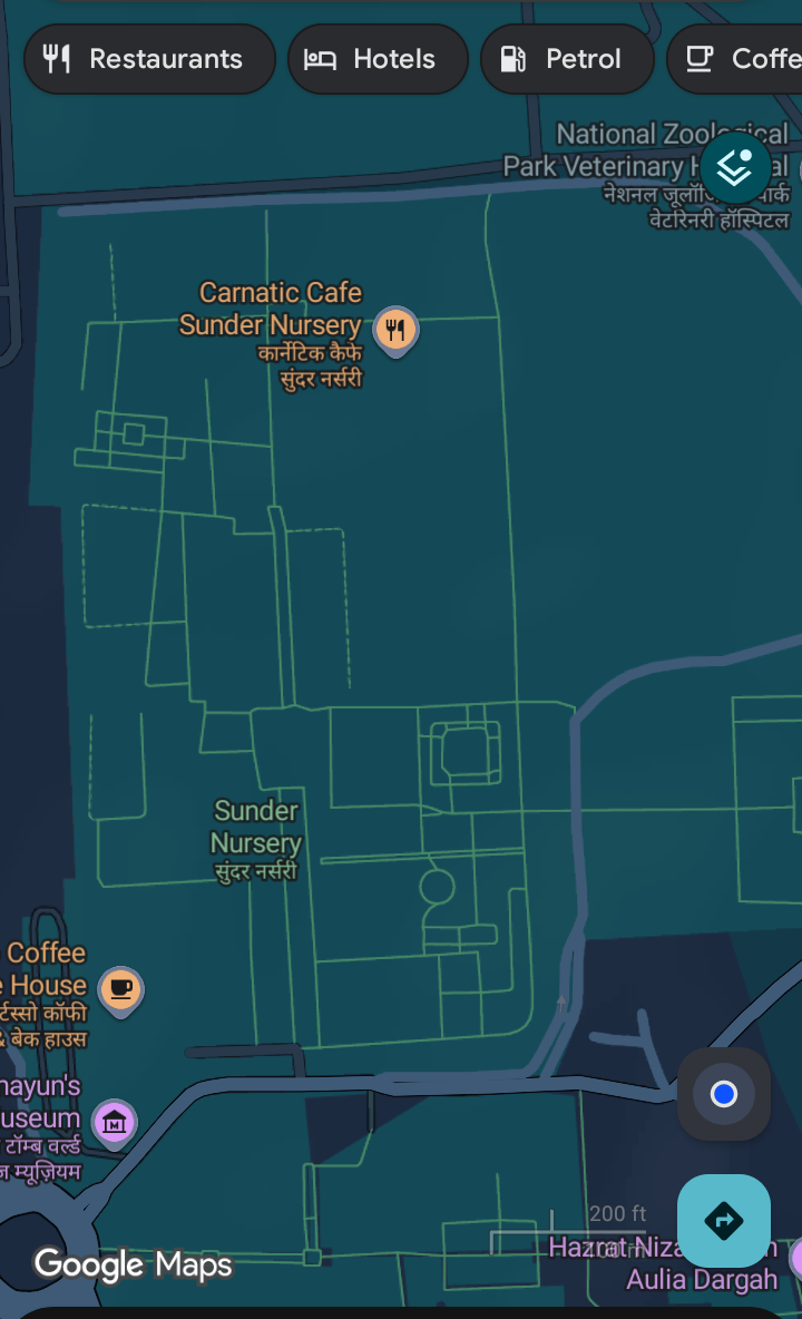 A Google Maps screenshot showing a map area with several location markers and interface elements. The top of the map features dark gray buttons labeled "Restaurants" (with a fork icon), "Hotels" (with a bed icon), "Petrol" (with a fuel pump icon), and "Coffee" (with a coffee cup icon). The map displays labeled locations including "Carnatic Cafe" with a fork icon, "Sunder Nursery" (with both English and Hindi text: "सुंदर नसरी"), "National Zoological Park Veterinary Hospital" (with Hindi text: "नेशनल जूलोगिकल पार्क वेटरिनरी हॉस्पिटल"), "Hazrat Nizam Aulia Dargah", and "Coffee House" (with Hindi text: "कॉफी हाउस"). The map uses a dark blue background with green street outlines. Interactive elements include a blue circular dot indicating the current location and a blue arrow button for directions at the bottom right corner. The Google Maps logo is visible at the bottom left.