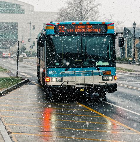 Blue bus with a bike rack in front is driving towards us in heavy snow with a digital sign that reads: 52 CAROLINE VIA BROOKTONDALE