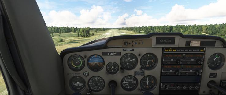 The cockpit dashboard of a Cessna aircraft shows a clear view of the instrument panel and the runway ahead. The central panel includes an airspeed indicator reading 55 knots, an attitude indicator showing the aircraft level, an altimeter, a turn coordinator, a heading indicator, and a vertical speed indicator. Two radio stacks display frequencies 132.650, 124.850, 110.50, and 113.90. The aircraft registration D-MJXY is visible above the center console. Outside, the runway stretches straight ahead, flanked by green fields and clusters of trees under a partly cloudy sky. The scene suggests the aircraft is either preparing for takeoff or in the early stages of landing.