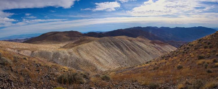 Rolling hills with dry yellow foliage in the foreground and dark mountain peaks in the background