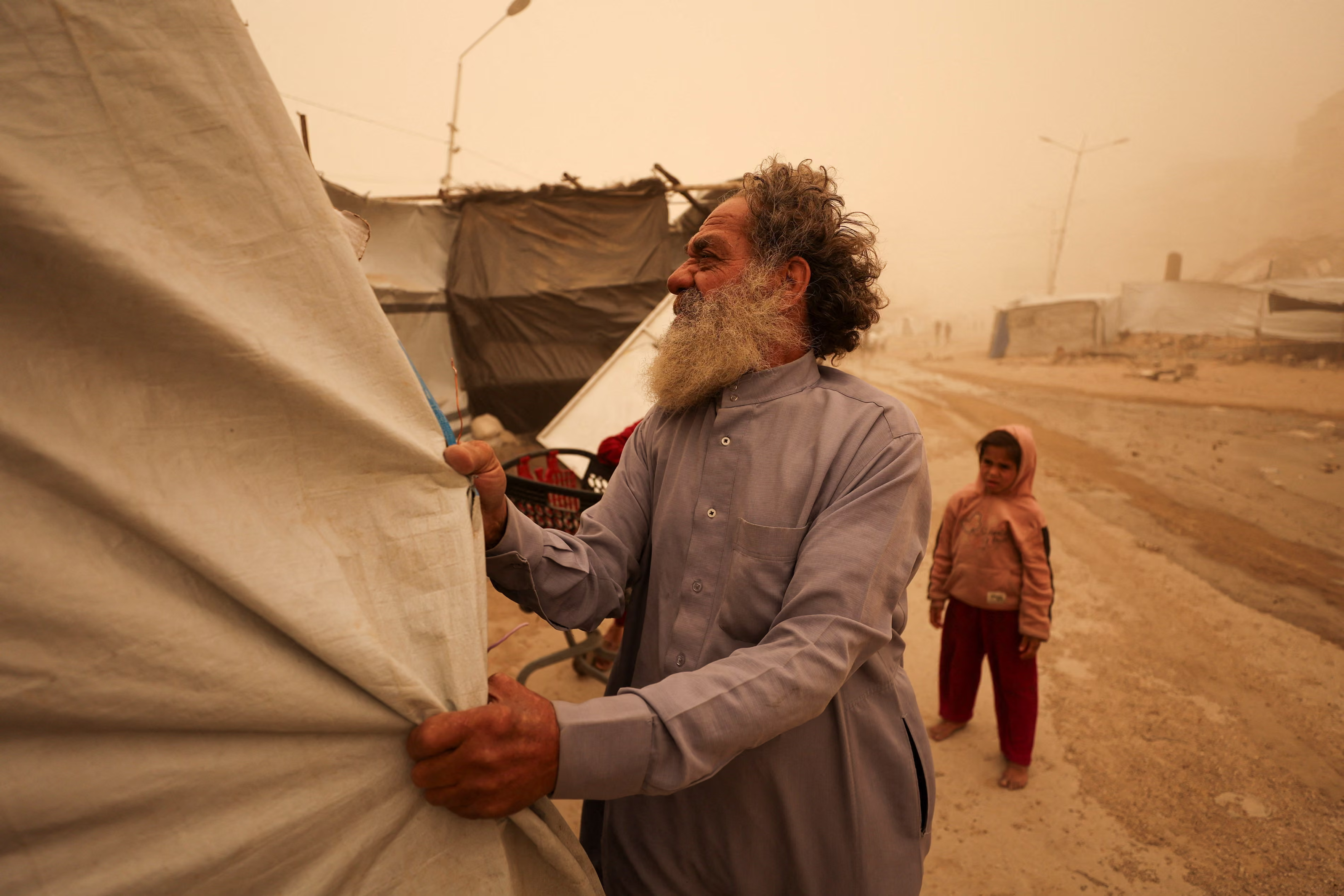 A man is fixing a tent in a sandstorm, with a child looking on.