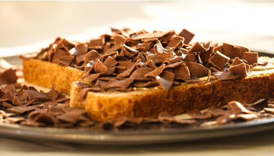 A slice of bread lies trapped under an avalanche of chocolate flakes that look like bark that has been scraped off a dying tree.