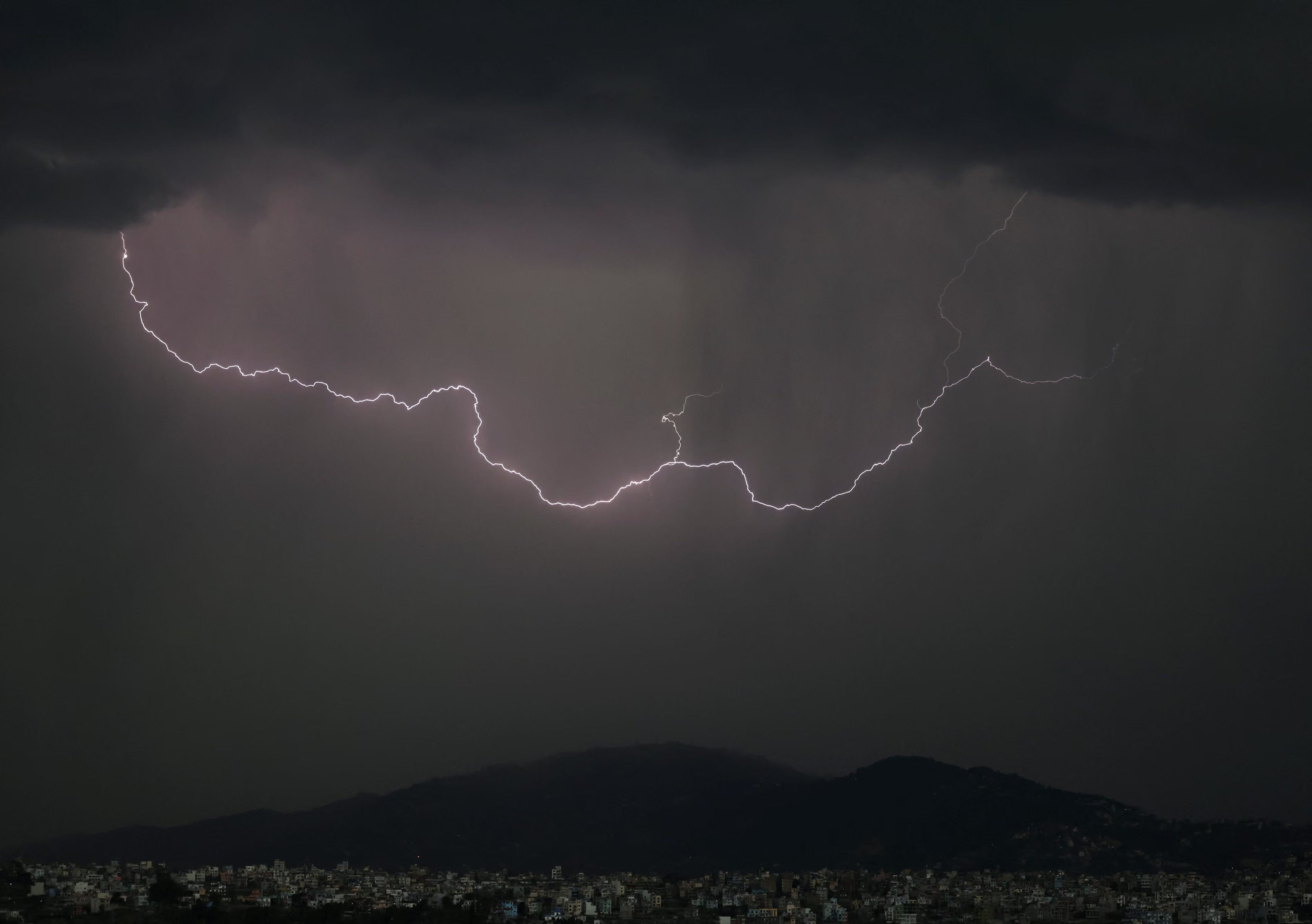 A lightning bolt strikes across the sky during rain.