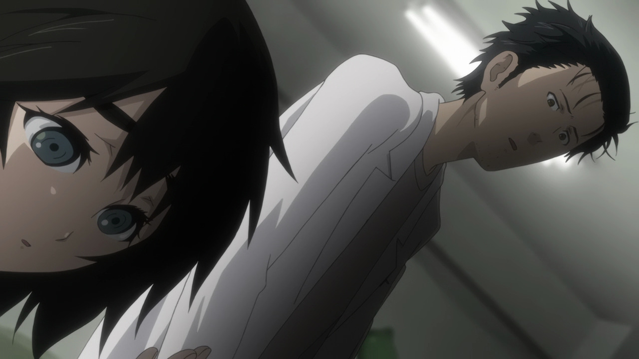 A girl (Mayuri) looking down at a pocket watch out of frame while a man (Okabe) looks worried behind her.