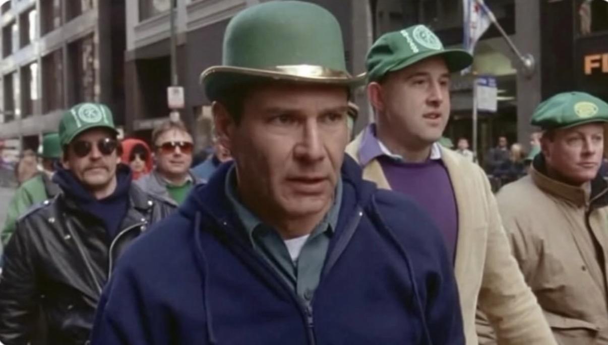 Harrison Ford in a still from The Fugitive, walking in the St. Patrick’s Day parade looking deeply uncomfortable.