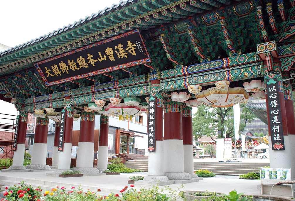 a very large gateway, extensively detailed with designs, golden letters on a large plaque on the front, seen from the front in a three quarter view, the sky cloudy