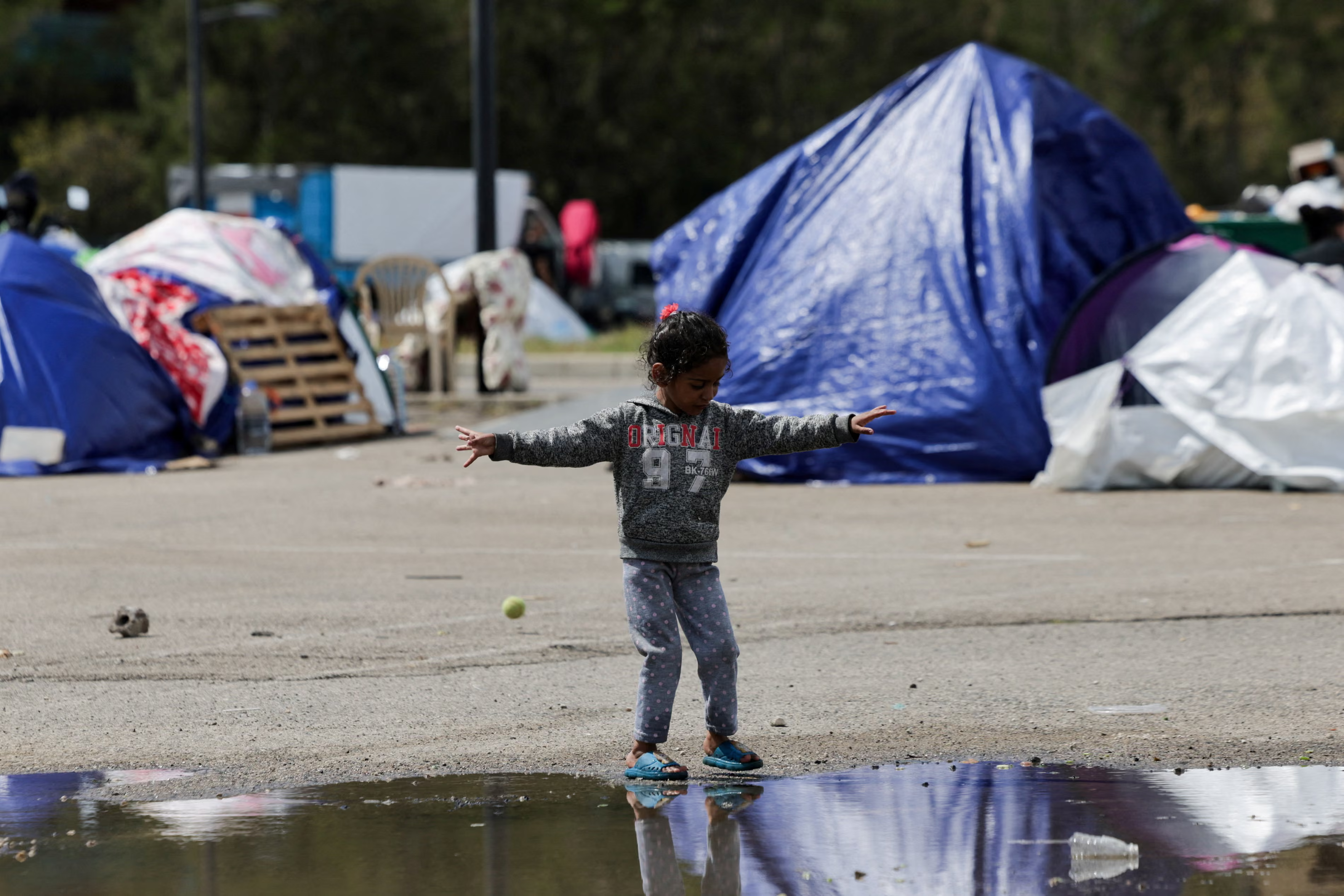 A displaced girl plays near a puddle.