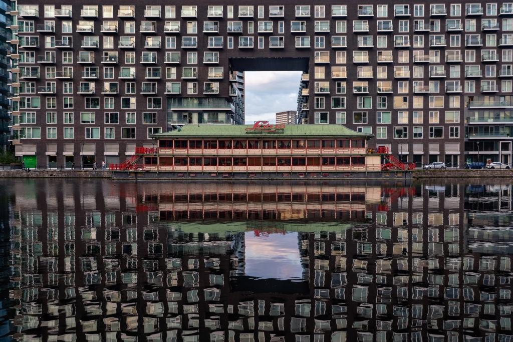 A low level pavilion and a hig-hrise residential building reflected in water.