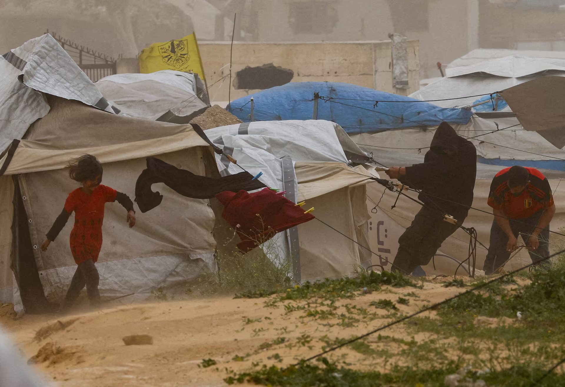 Displaced Palestinians try to repair a tent during a sandstorm at a tent camp.