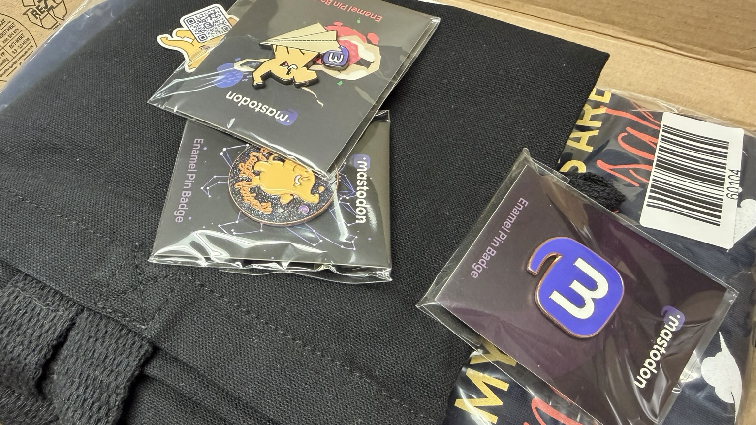 Photo of Mastodon Pins, tote bag, and t-shirt pile.