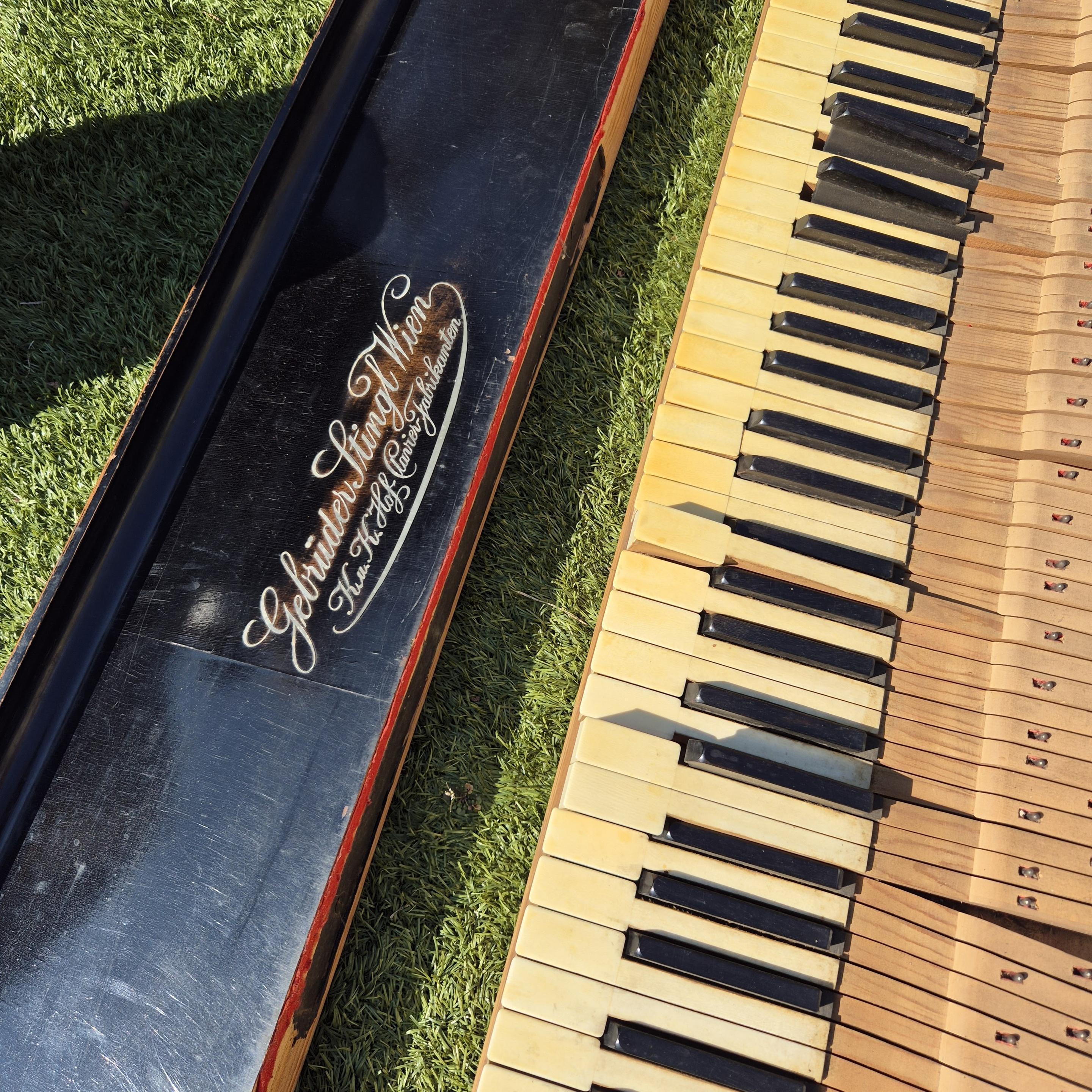 Keyboard and keyboard cover of a grand piano, the keyboard cover says "Gebrüder Stingl Wien"