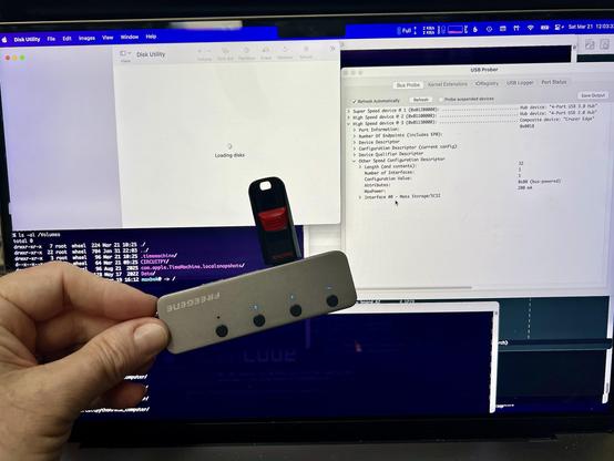 Me holding up a regular FAT-formatted USB thumb drive that works on every other system, but somehow flabbergasts Apple's MacOS. Behind it is my MacBook's screen showing USB Prober recognizing the drive but Disk Utility hanging. I love my Mac, but MacOS basic functionality has really gone down.
