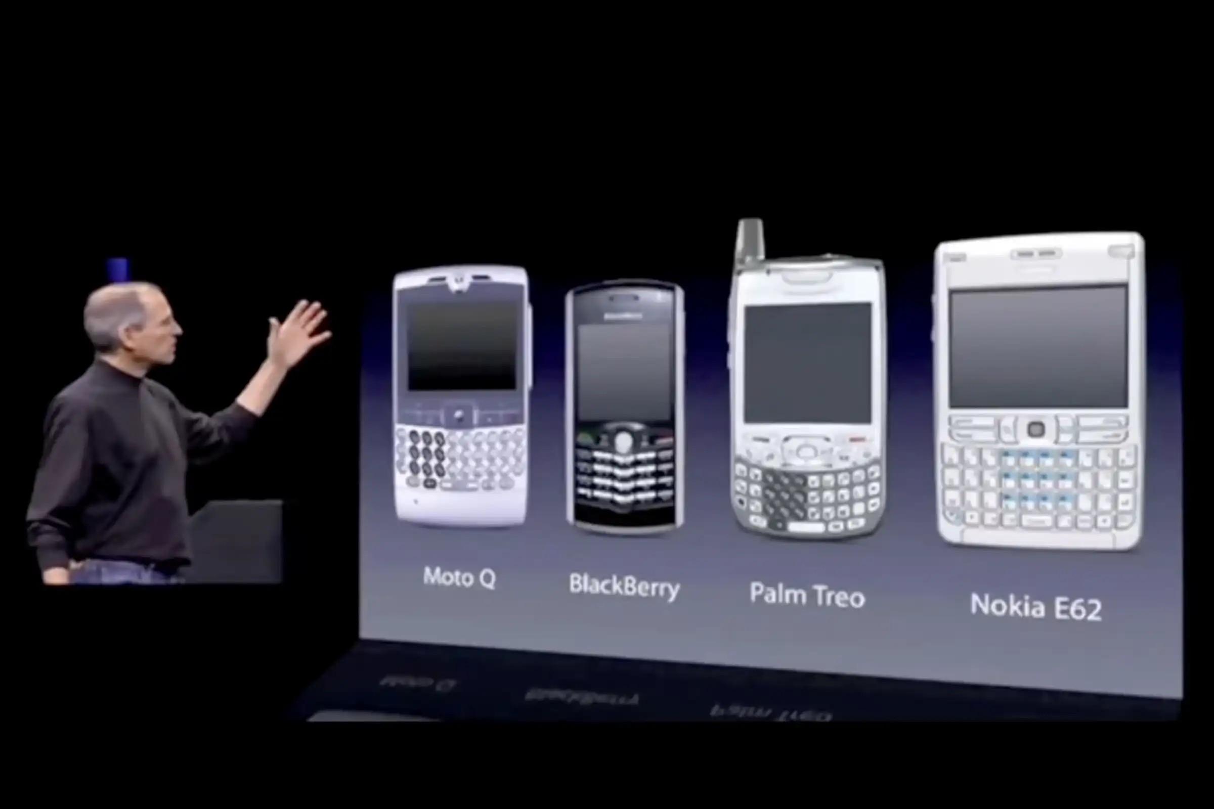Steve Jobs on stage pointing to the current smart phone devices in the market including Blackbeerys.