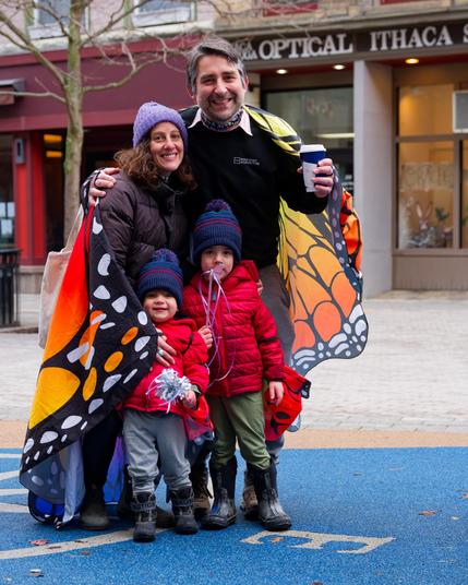 A man and woman both wearing monarch wing capes post with two children wearing matching red coats