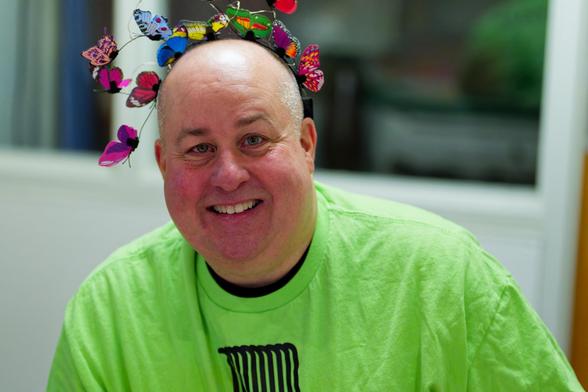 Man with lime green shirt and butterfly headdress at Ithaca Fairy Festival with a window to a dark space in the background