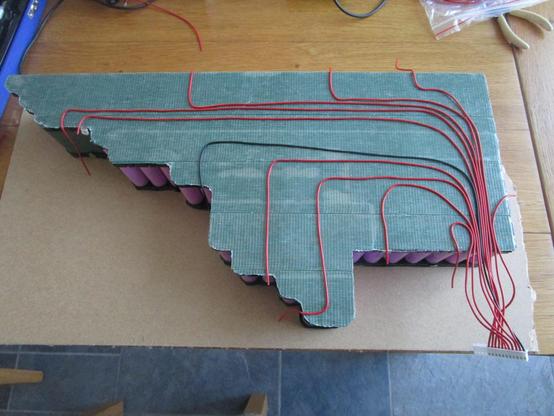 grey battery pack full of pink cells fed by a network of red and black wires on a wood grain table