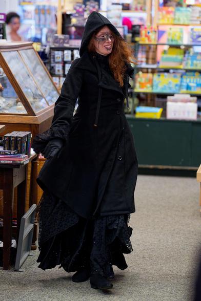 Woman with heavy black cloak with a hood has light brown hair and painted face
