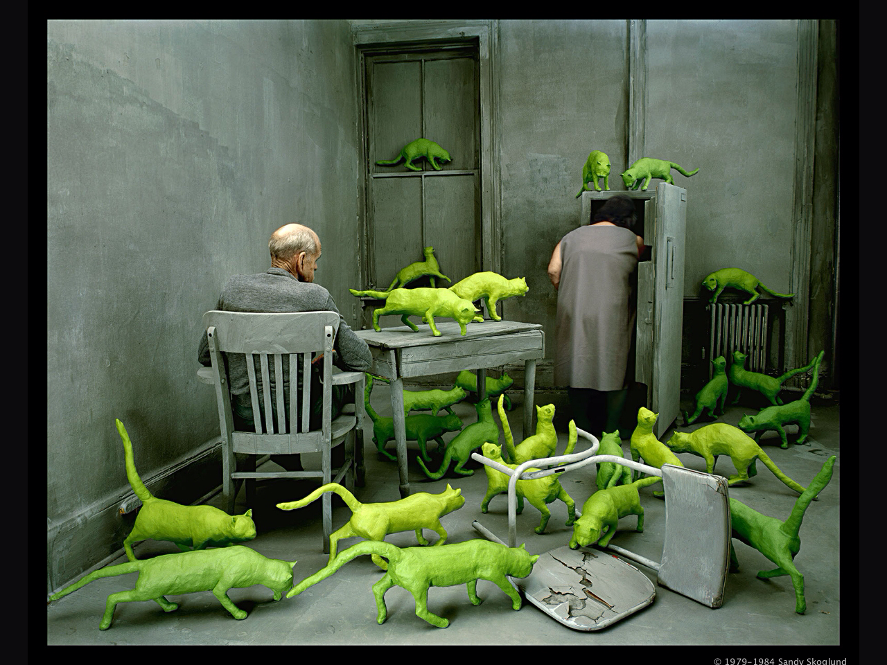 Radioactive Cats by Sandy Skoglund, 1980. Photo showing sculptural cats, in day-glo green circling a man and woman in an all grey room.