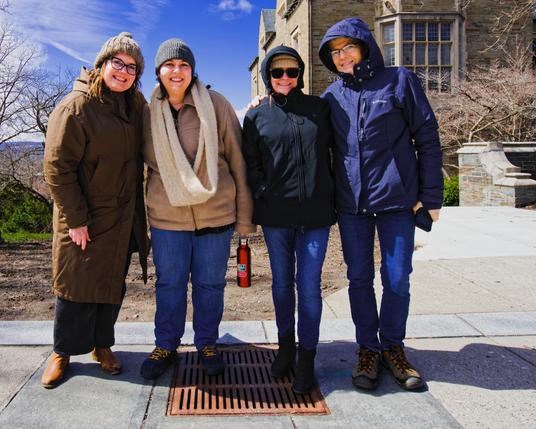 Four white women pose with the sun to the left and a big building that looks like a castle to the right