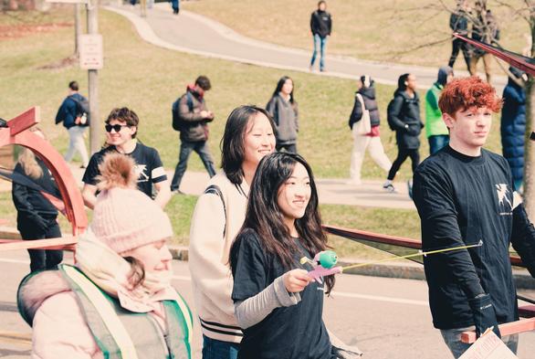 Several students are carrying segments of a dragon in front and in back while more students walk behind them