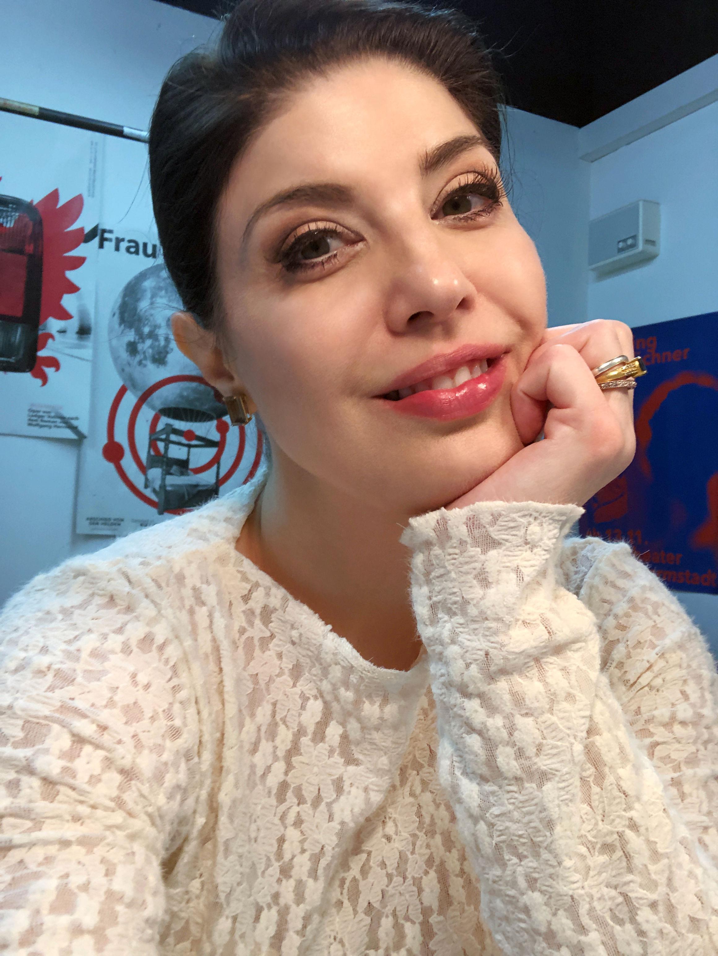 Selfie portrait of a woman with dark hair styled into a chic updo, red lipstick, and false eyelashes, looking directly at the camera. She is wearing a fluffy white lace top with a boat neckline and long sleeves, and is resting her chin on her left hand. Megan Marie Hart in her dressing room at the Staatstheater Darmstadt after the premiere of Felix Weingartner’s opera “Kain und Abel” on March 28, 2026. CC BY-SA 4.0