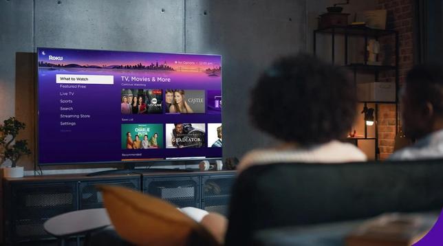 A couple is sitting in a dark room, with concrete walls, bricks, and industrial furniture. Watching TV with Roku.