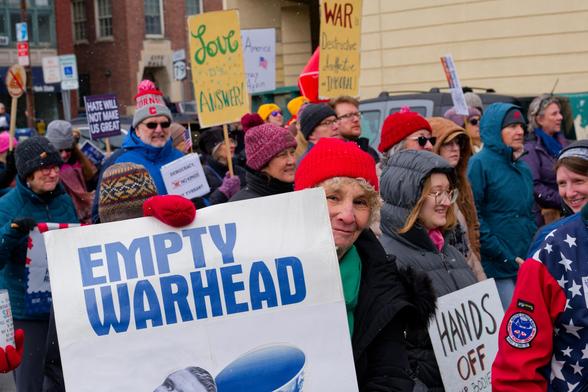 Woman in near field holds a sign that says EMPTY WARHEAD in front of a big crowd with numerous people holding more signs