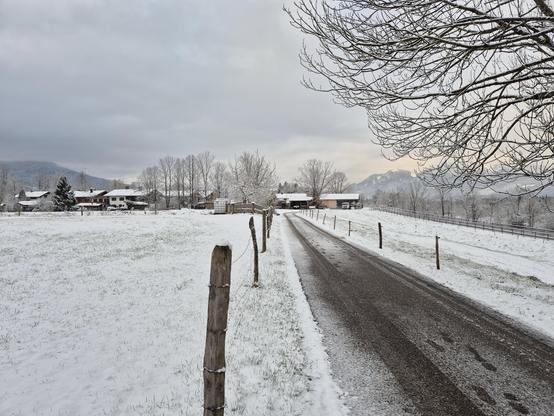 A snow covered meadow and a rural street leading into the back. The sky is covered in clouds.